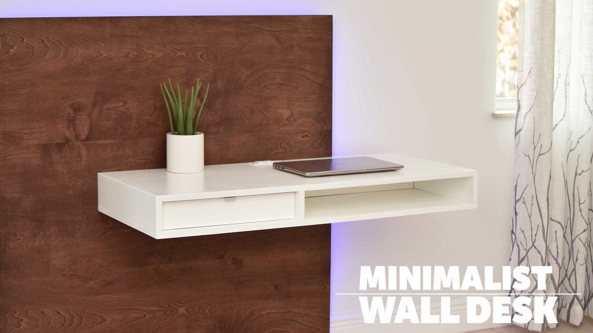 A white wall-mounted desk with a drawer and an open slot is attached to a wooden panel. The surface holds a small potted plant and a closed laptop, demonstrating possible use. The words “MINIMALIST WALL DESK” appear in the lower right corner.